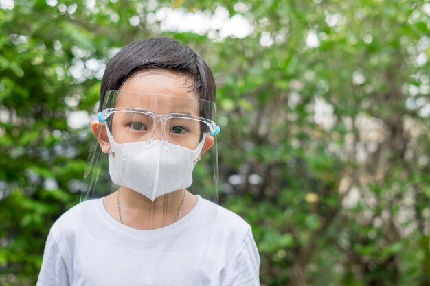 Asian boy wear mask and face shield at home garden