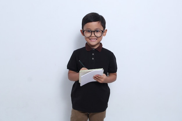 An Asian boy wearing a black tshirt and glasses is looking ahead while holding a notebook