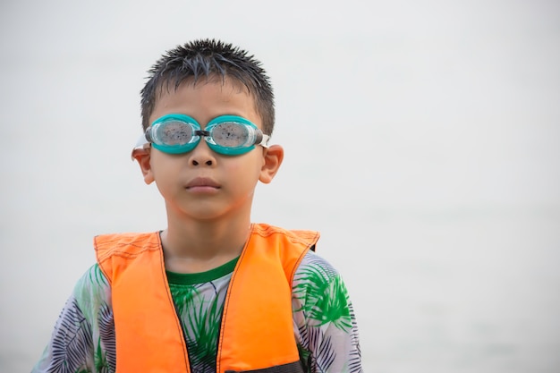 ライフジャケットと水泳ゴーグルを身に着けているアジアの少年