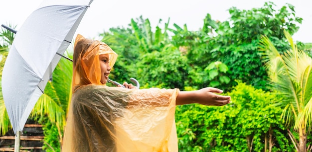 Asian boy wearing orange raincoat holding umbrella happy and having fun in the rain on a rainy day