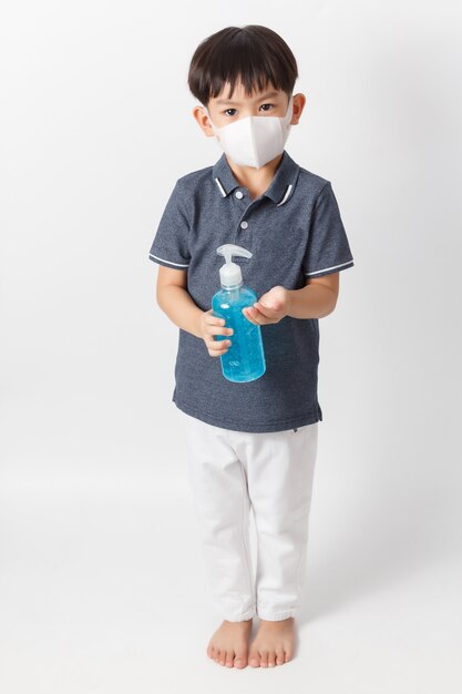 Asian boy wearing a protection mask and holding bottle of alcohol gel for cleaning hands.