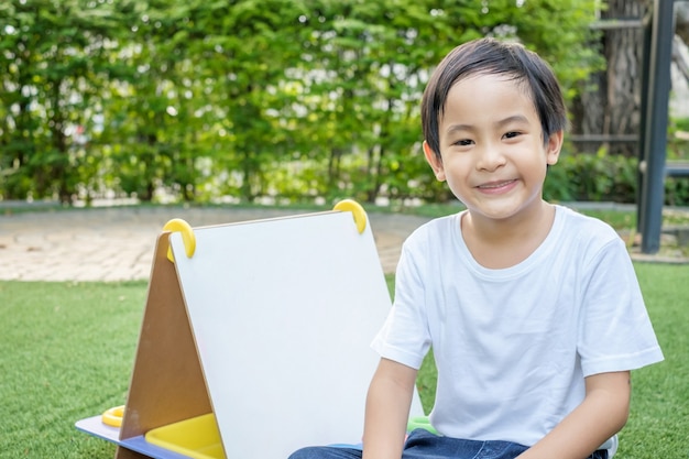 An Asian boy in a white t-shirt and jeans is sitting on the lawn