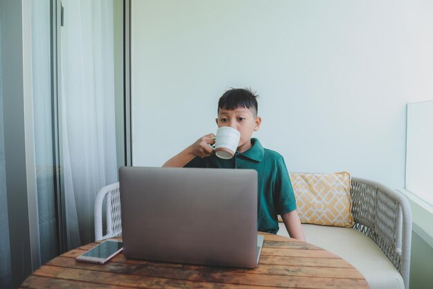 Азиатский мальчик, который хочет пить во время просмотра онлайн-трансляции на ноутбуке