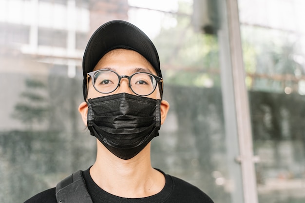 Asian boy with glasses and black respiratory mask protects himself on the street from coronavirus