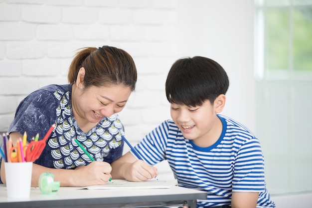 母親の家庭であなたの宿題を教えて学ぶアジアの少年