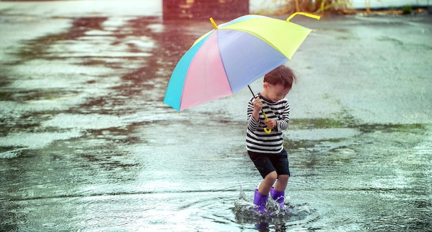 雨の中でジャンプする傘を持つアジアの少年