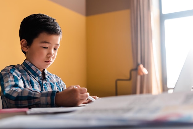 Asian boy writing and studying online with laptop at home during quarantine