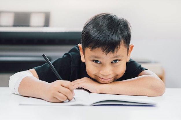 傷ついた手のアジアの男の子がノートを書いている