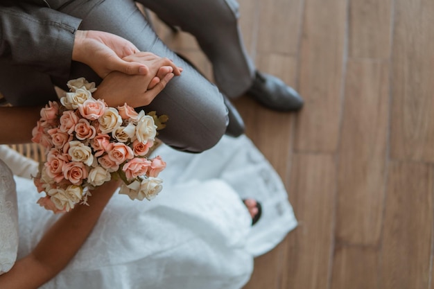 写真 アジアの花嫁が一緒に椅子に座り、花嫁に花束を持って手をつないでいます