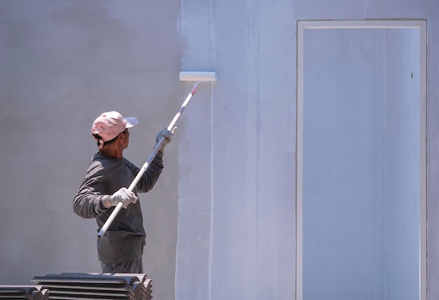 주택 건설 현장 내부의 콘크리트 벽에 흰색 프라이머를 칠하는 아시아 건축업자