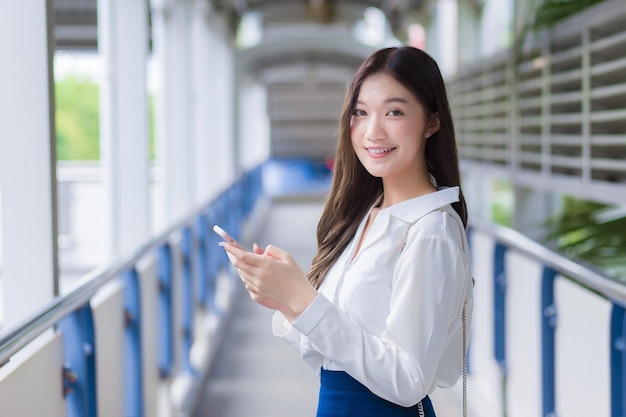 Asian business beautiful woman stands on flyover of skytrain in town while uses her smartphone