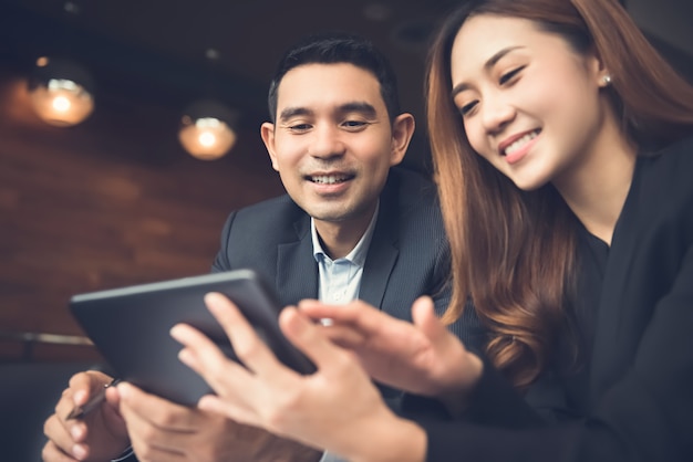 Asian business couple enjoying using tablet computer surfing internet in cafe 