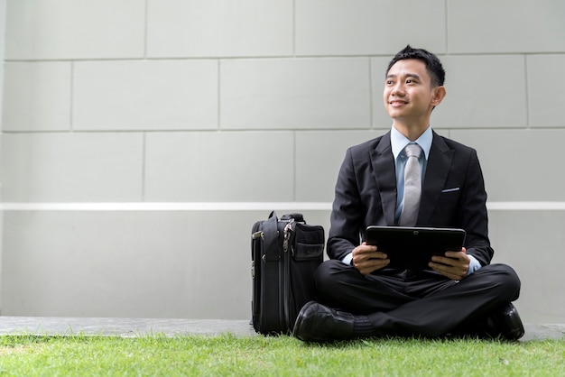 Asian business male using portable computer on park of city. He is looking