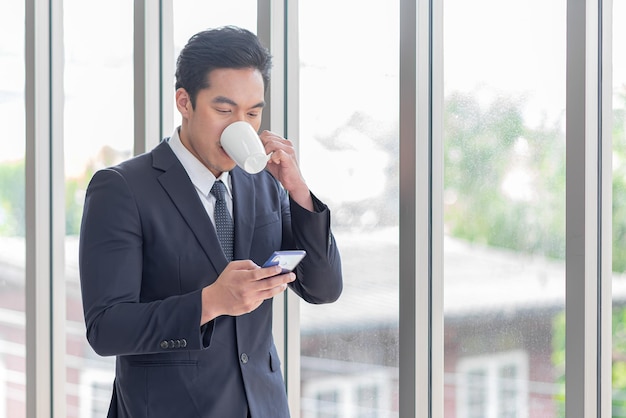 アジア系のビジネスマンがコーヒーを飲み、携帯電話を使う