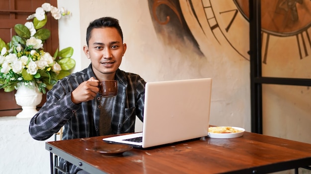 アジアのビジネスマンがカフェでノートパソコンでコーヒーを飲む