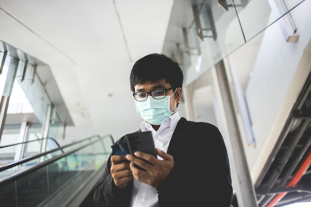 asian business man in glasses and wearing surgical mask paying for online services with credit card