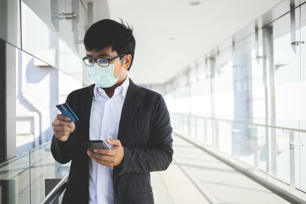 asian business man in glasses and wearing surgical mask paying for online services with credit card