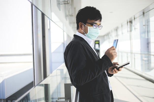 Asian business man in glasses and wearing surgical mask paying for online services with credit card