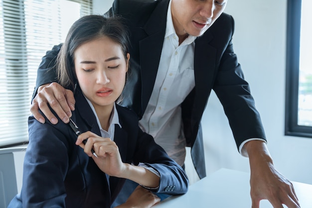 アジアビジネスの男性は彼の手を抱擁同僚女性を使用して、オフィスでの仕事、性的暴行および嫌がらせの概念を説明します