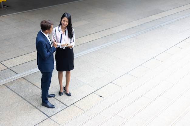 Asian business man and young beautiful woman working on digital tablet computer standing outside office building.