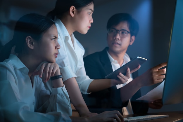 Asian business people working hard late together and planning with computer in office at night, success achievement teamwork concept.