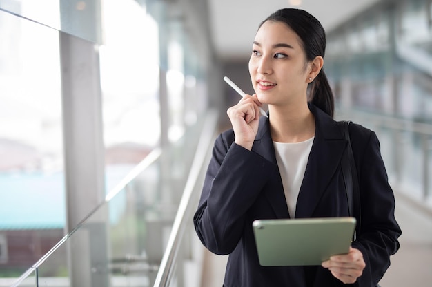 Фото Азиатская деловая женщина, держащая планшет, глядя в сторону, умная бизнес-концепция.