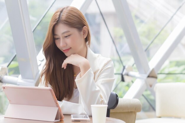 彼女はコーヒーショップに座っている間、アジアのビジネスウーマンは彼女の手でタブレットを見ています