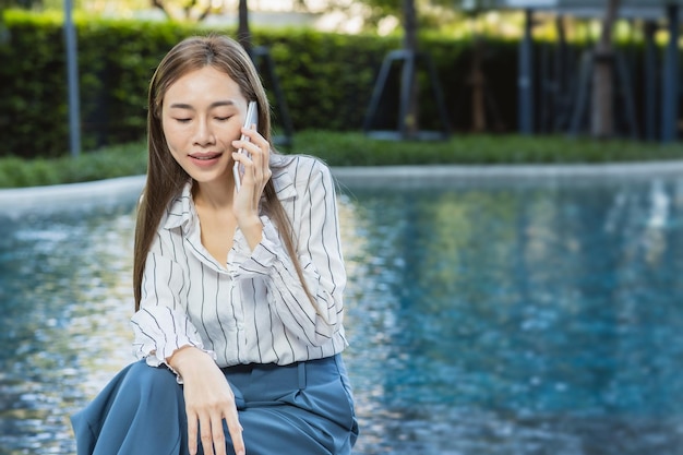 屋外の緑の自然プールの背景を呼び出すアジアのビジネス女性中年電話