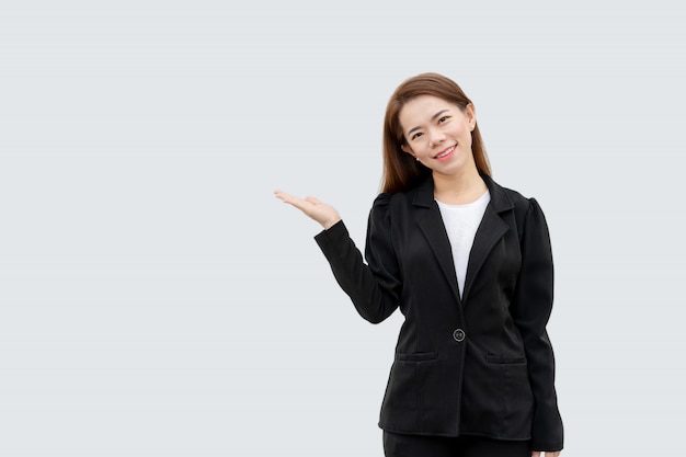 白い色に分離された黒のスーツで長い髪の手を提示するアジアビジネス女性