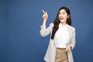 Asian business woman smiling and pointing to empty copy space isolated on deep blue background