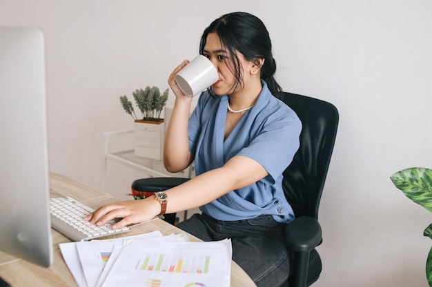 Asian business woman working with a computer while drinking glass of water on a desk in the office