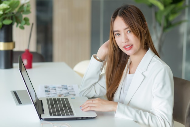 Asian business woman works in coworking space with laptop paper work while looking at the camera