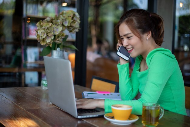 Asian Business women are using mobile and touch smart phone for Communication and women using notebook for working in coffee shop