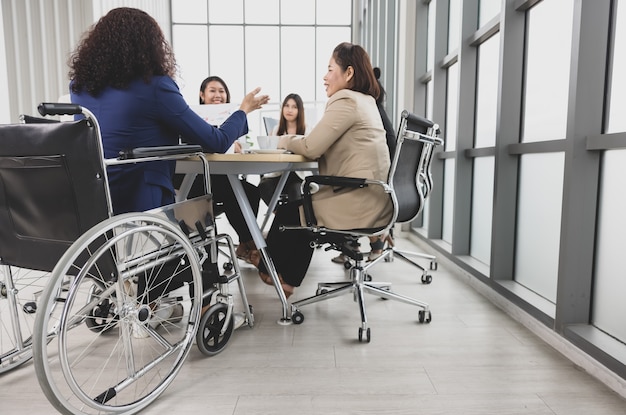 Asian business women and handicap woman sitting on wheelchair are in meeting together on the table in office. Concept for business meeting.