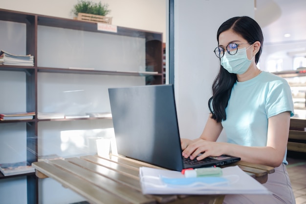 Asian business women working at home wearing medical masks Asian businesswoman in quarantine zone for coronavirus wearing protective mask Work from home Clean her hands with a cleaning gel.