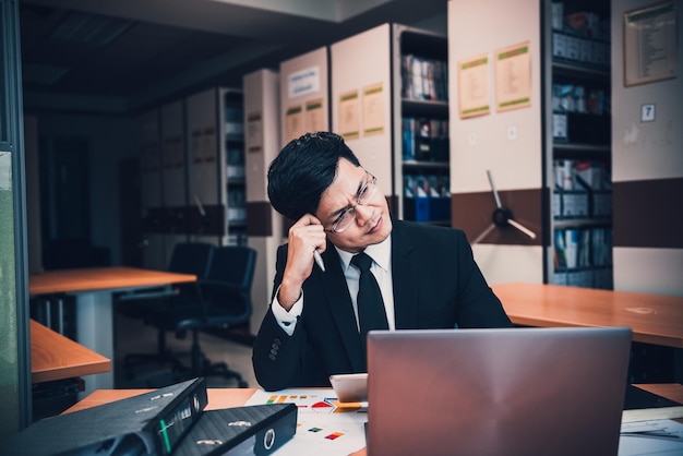 Asian businessman in black suit think idea for work at officehe work overtime alone in a companydark tonethailand people