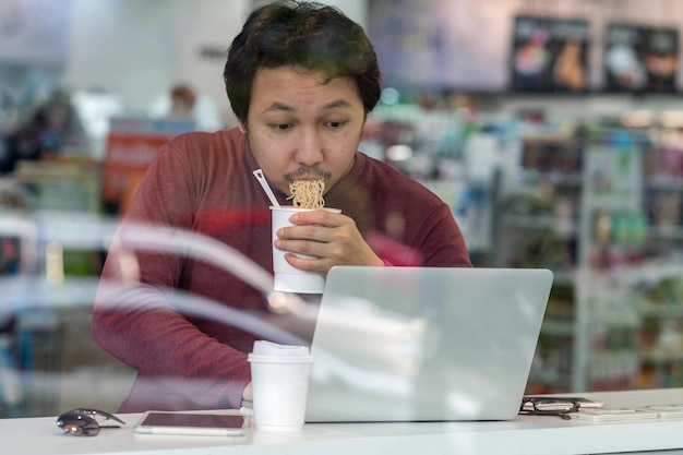 Asian businessman in casual suit eating noodles with urgent action in rush hour at the desk