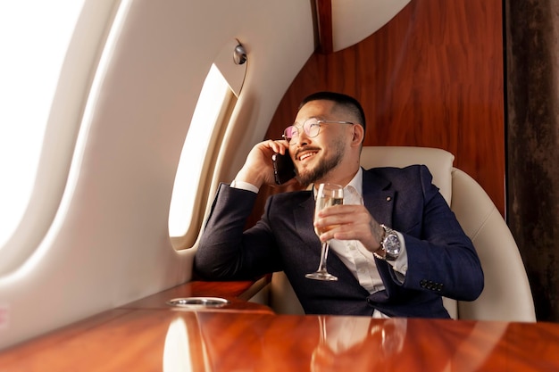 Foto l'uomo d'affari asiatico vola in un jet privato di lusso, parla al telefono e beve champagne