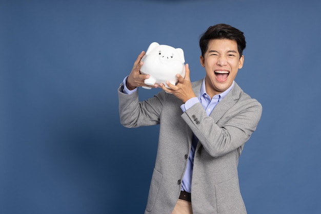 Asian businessman holding white piggy bank isolated on blue background