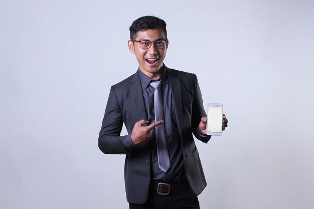 An Asian businessman holds and points to a blank screen smartphone with an excited expression