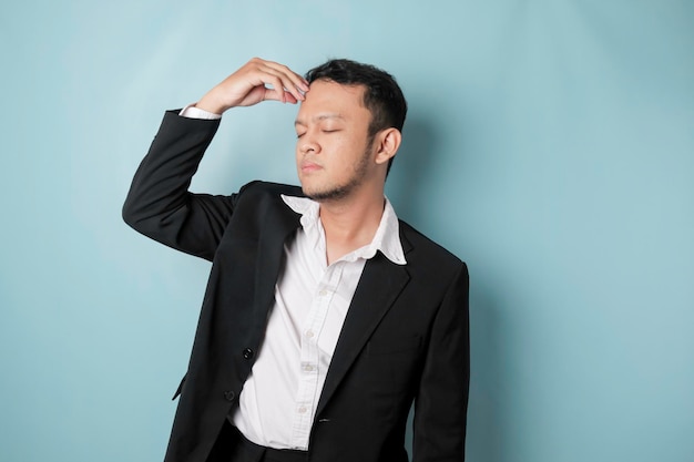 Asian businessman looks tired and depressed has a sad expression while holding his head Isolated blue background