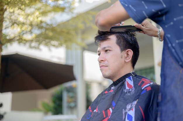 Asian businessman making haircut at home. Outdoor barbershop in garden. Social distancing and New normal lifestyle.