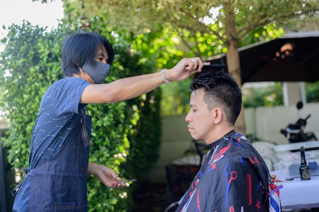 Asian businessman making haircut and salon at home. Outdoor barbershop in garden. Social distancing and New normal lifestyle.