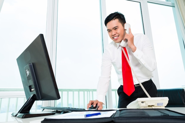 Asian businessman on phone working in office on computer