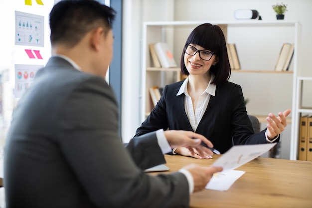 Asian businessman presents report to caucasian businesswoman in meeting