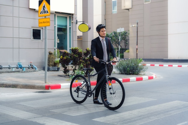 L'uomo d'affari asiatico spinge una bicicletta attraverso un attraversamento pedonale