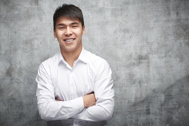 Asian businessman in shirt over gray background. Portrait of a successful smiling Kazakh entrepreneur with arms crossed