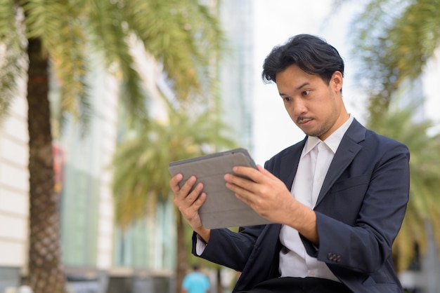 Uomo d'affari asiatico seduto all'aperto in città utilizzando un computer tablet digitale