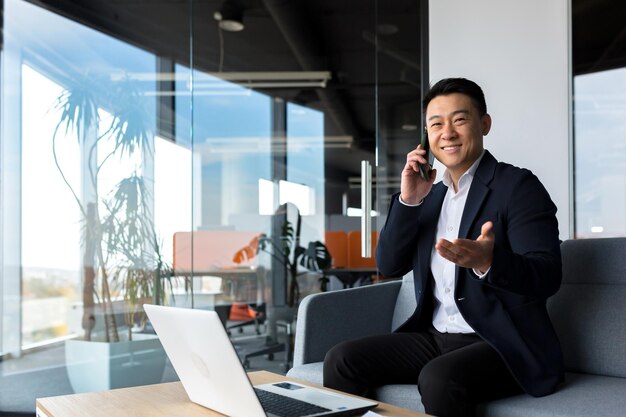 Asian businessman smiling and rejoicing happy talking on the phone freelancer man in modern office looking at camera