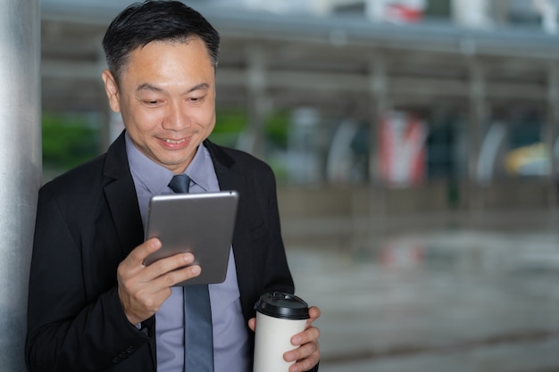 Asian Businessman standing and holding digital tablet with business office buildings in the city